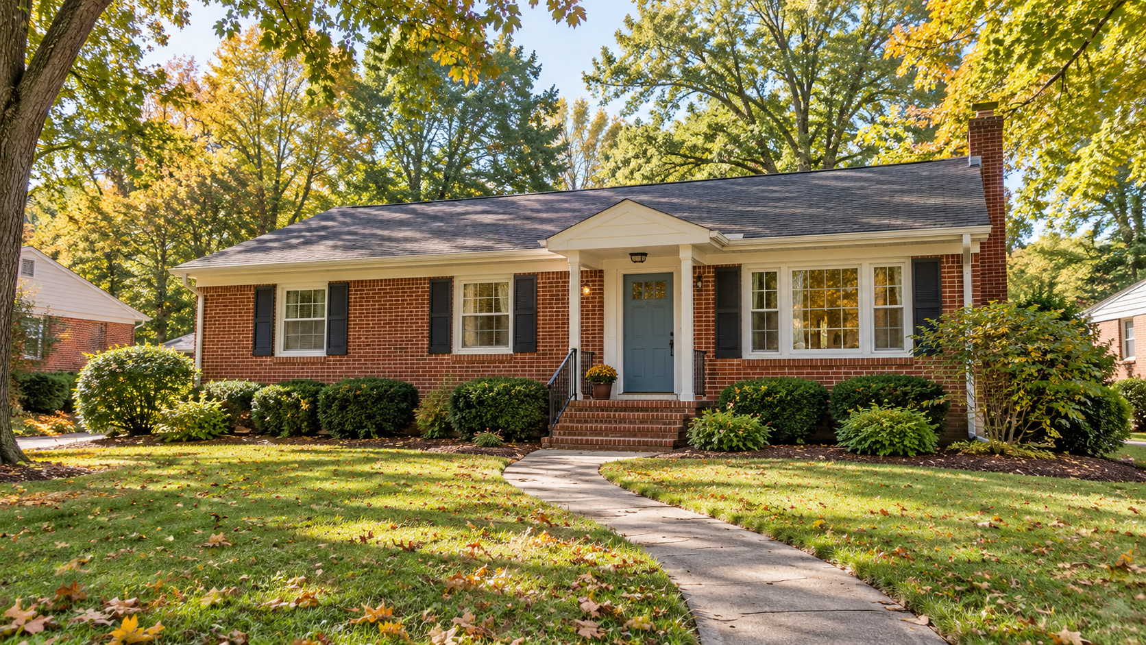 Modest brick ranch home with a blue front door and curved walkway, framed by trees with autumn foliage.